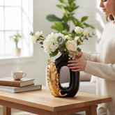Home Sajawat black ceramic vase with gold leaf detail and white floral arrangement on a wooden table