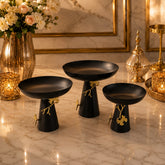Home Sajawat set of three matte black pedestal bowls with gold ginkgo leaf accents on a marble surface.