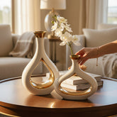 Home Sajawat set of two modern ceramic vases with glossy white exteriors and reflective gold interiors on a table.