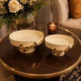 Home Sajawat set of two cream metal serving trays with gold floral butterfly accents on a dark wood coffee table.