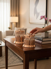 Home Sajawat glass storage jars with gold lattice metalwork and floral lids on a wooden table in a living room