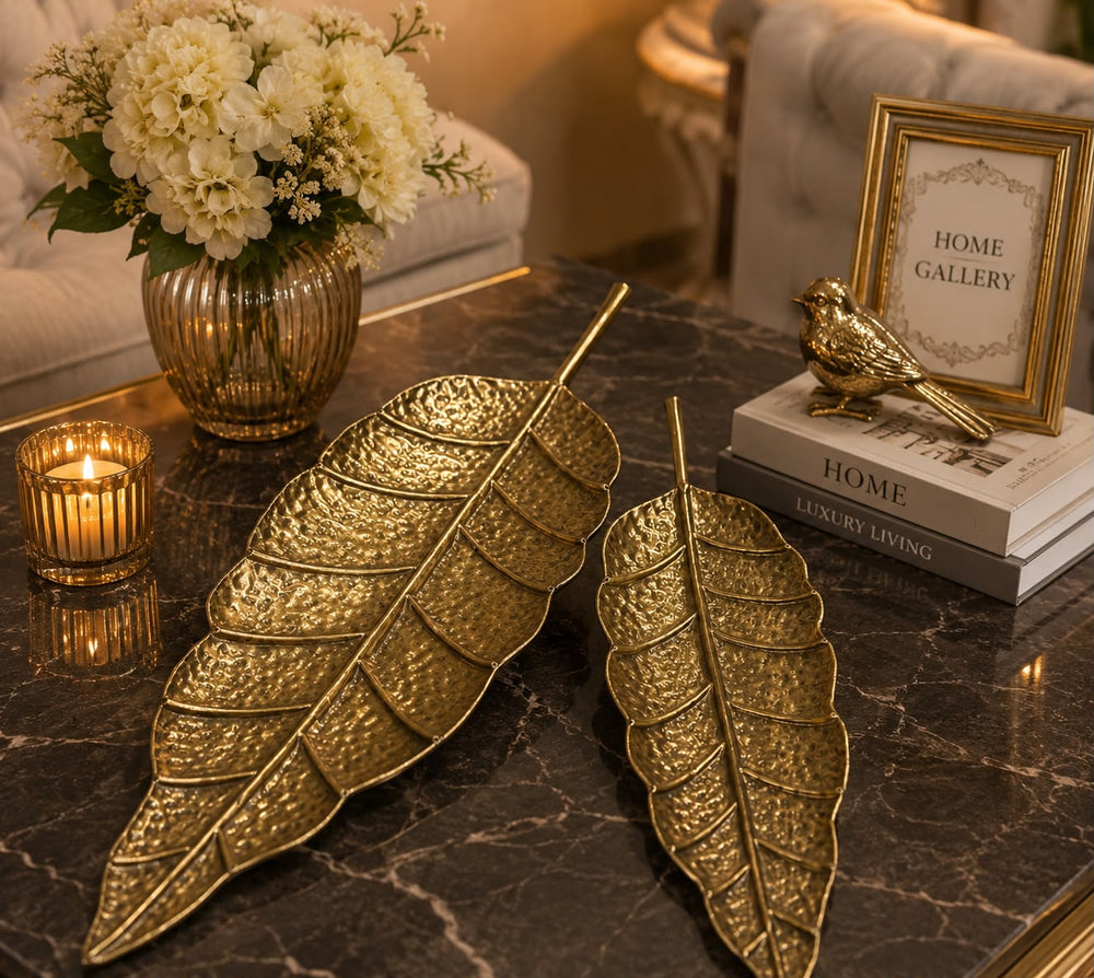 Home Sajawat set of two gold hammered metal leaf-shaped decorative trays on a dark marble coffee table.