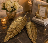 Home Sajawat set of two gold hammered metal leaf-shaped decorative trays on a dark marble coffee table.