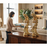 Home Sajawat set of two gold and white peacock statues with teal gemstone accents on fluted pedestals in a living room.
