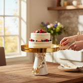 Home Sajawat gold and white pedestal cake stand with butterfly accents holding a berry-topped cake on a wooden table.