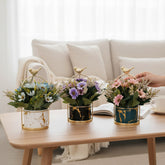 Home Sajawat artificial flower pots with marble-effect ceramic, gold bird accents, and colorful faux floral arrangements.