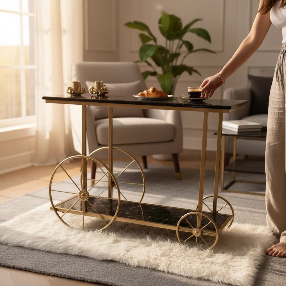 Home Sajawat black marble-effect serving cart with gold frame and decorative wheels. A croissant and coffee are on top.