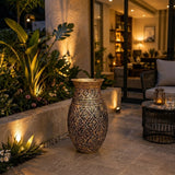 Home Sajawat ornate metallic floor vase with embossed patterns on a patio at night with warm ambient lighting.