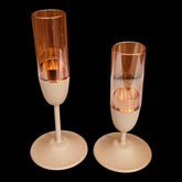 Home Sajawat set of two stemmed candle holders with matte beige bases and clear glass cylinders with copper inserts.