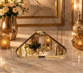 Home Sajawat triangular mirror serving tray with a polished gold metal frame on a marble table with candles.