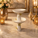 Home Sajawat white ceramic two-tier pedestal serving bowl with gold floral accents on a marble tabletop.