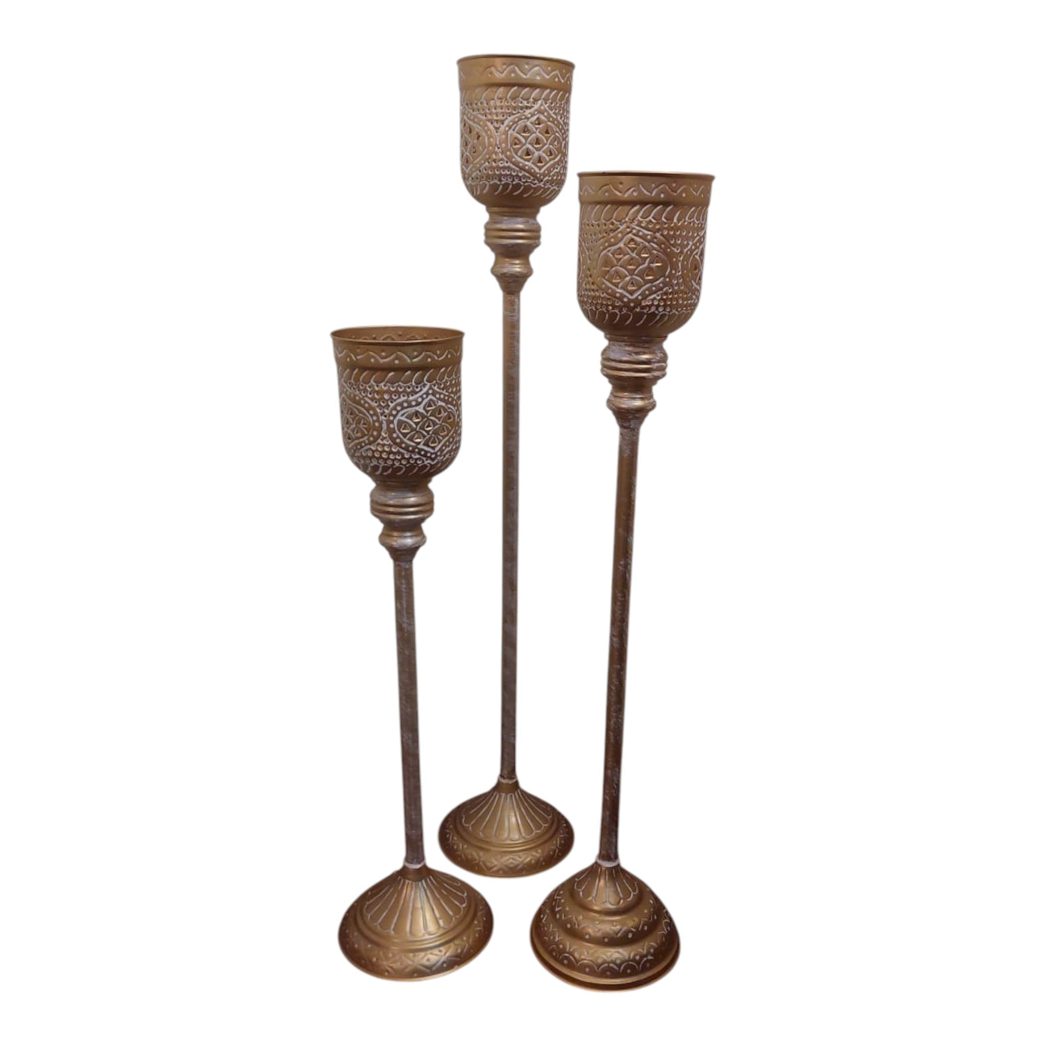Home Sajawat set of three tall antique gold floor candle holders with white ornate detailing and flared bases.