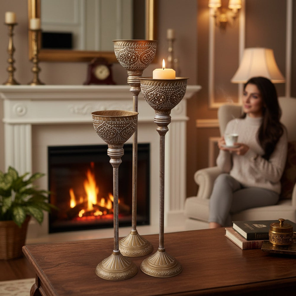 Home Sajawat set of three antique gold floor candle holders with white detailing and ornate cups. Tall, decorative stands with flared bases.