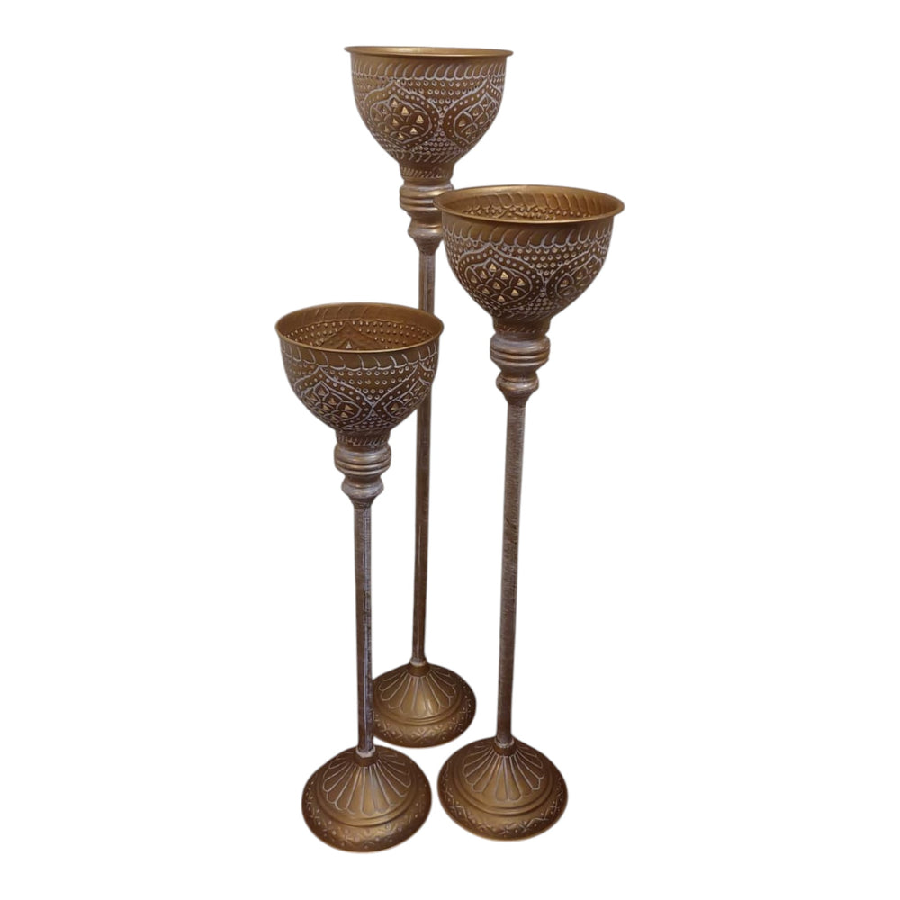 Home Sajawat set of three antique gold floor candle holders with white detailing and ornate cups and bases.