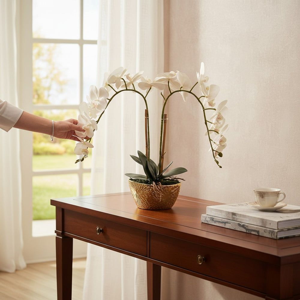 Home Sajawat artificial white Phalaenopsis orchid with silk blooms in a textured gold ceramic pot on a wooden table.