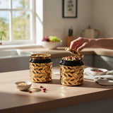 Home Sajawat set of two black and gold textured ceramic storage jars with soda-can style lids on a kitchen counter.