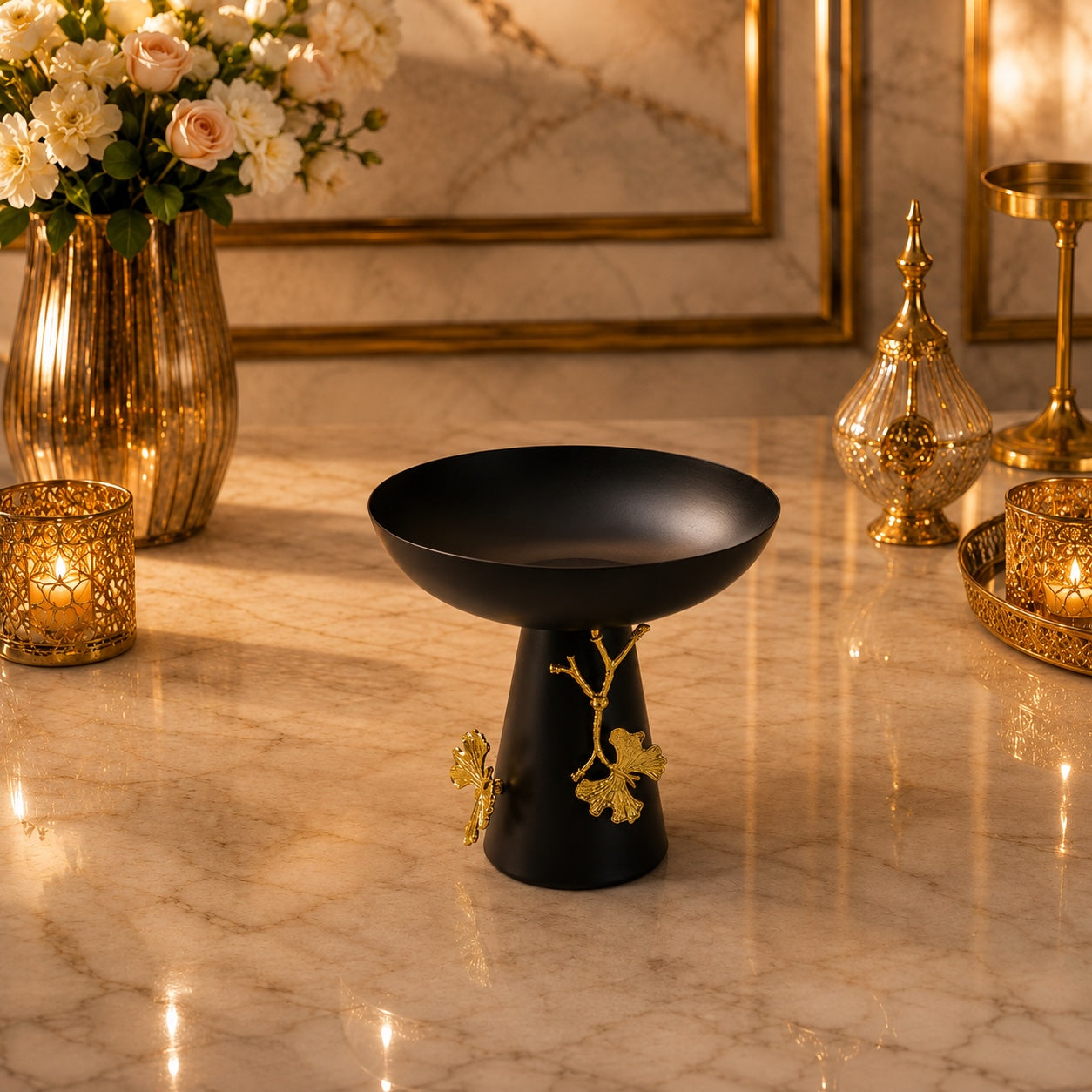 Home Sajawat matte black pedestal bowl with gold ginkgo leaf accents on a marble table with warm ambient lighting.