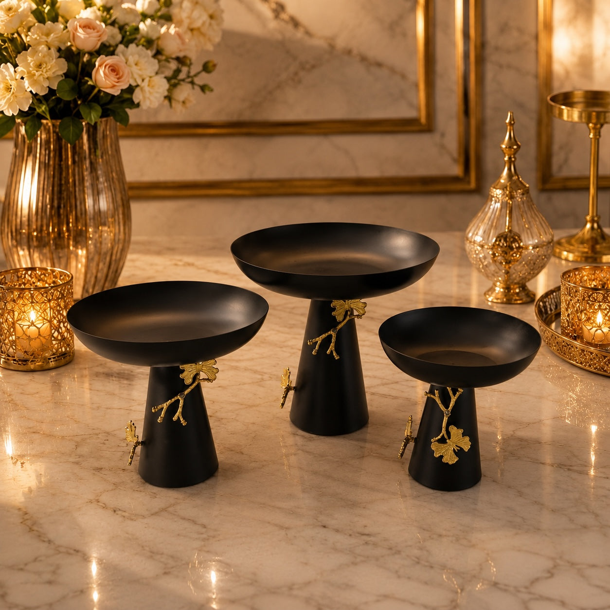 Home Sajawat set of three matte black pedestal bowls with gold ginkgo leaf accents on a marble surface.