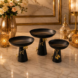 Home Sajawat set of three matte black pedestal bowls with gold ginkgo leaf accents on a marble surface.