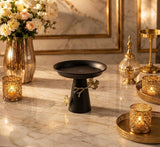 Home Sajawat matte black pedestal serving stand with gold branch and butterfly accents on a marble table.