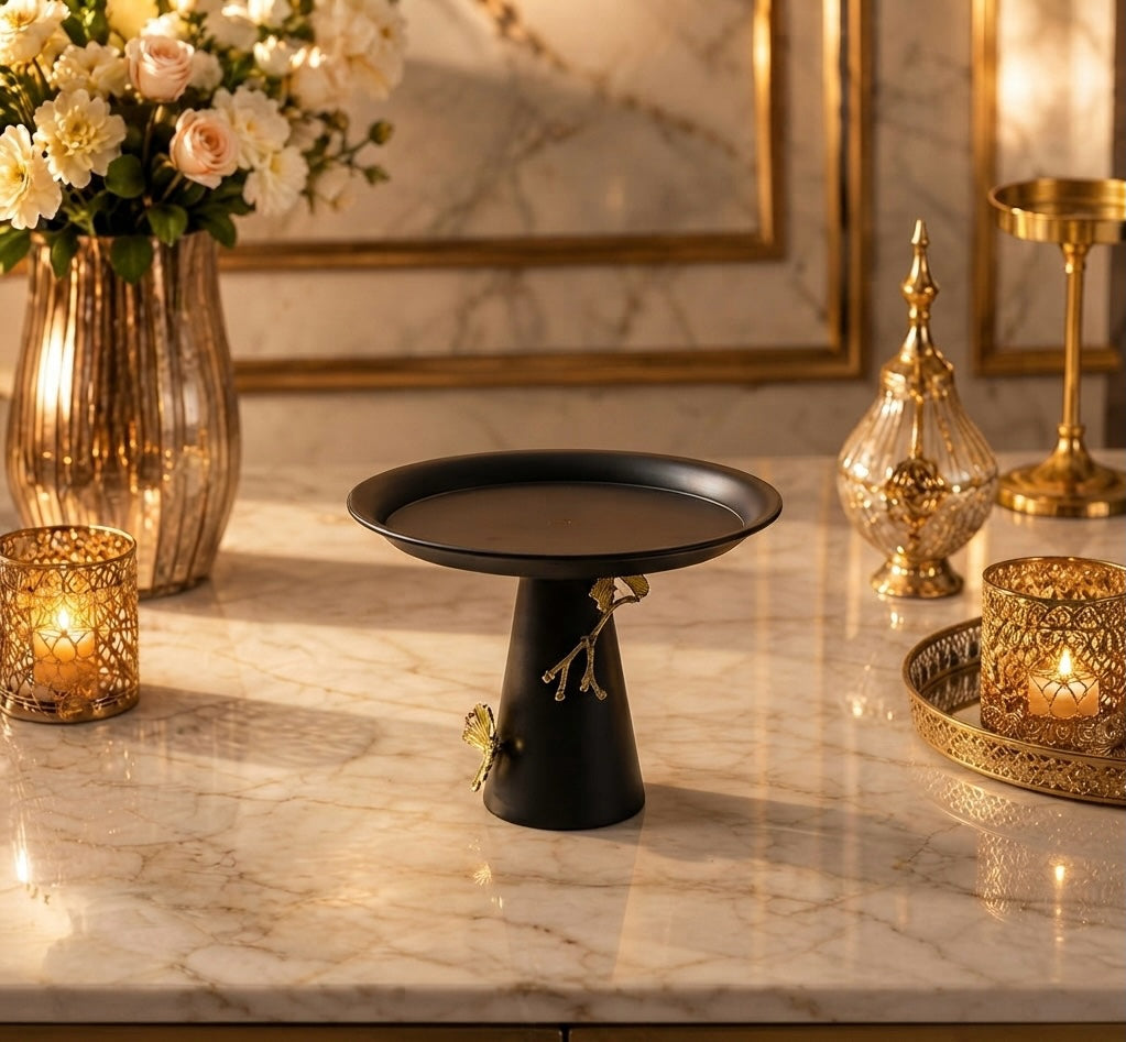 Home Sajawat matte black pedestal serving stand with gold branch and butterfly accents on a marble table