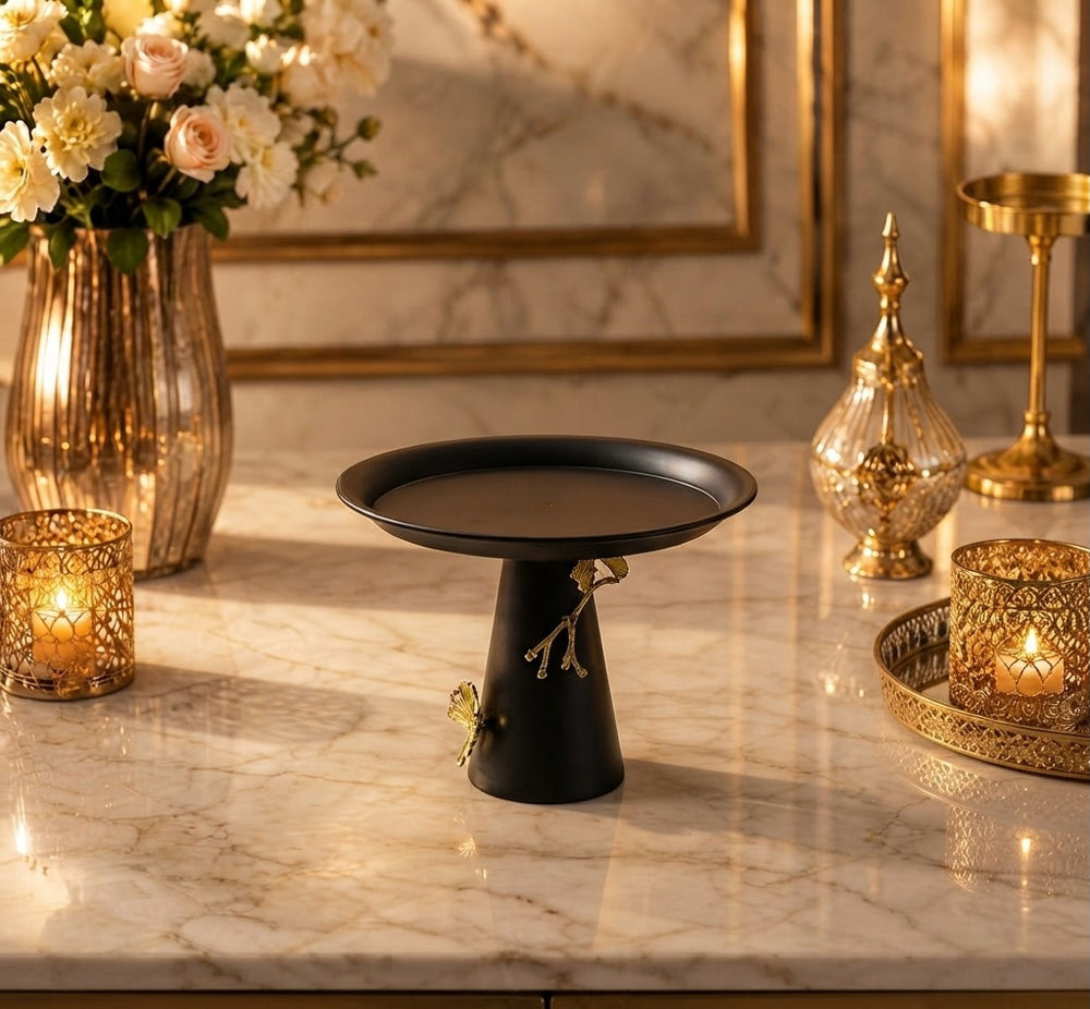 Home Sajawat matte black pedestal serving stand with gold branch and butterfly accents on a marble table