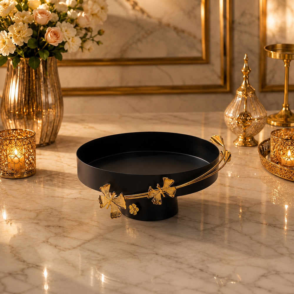 Home Sajawat matte black pedestal serving tray with elegant gold floral rim detailing on a marble tabletop