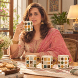 Home Sajawat ceramic coffee mug set with colorful geometric patterns and gold handles held by a woman at a table.