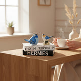 Home Sajawat decorative resin bird figurines in blue and white displayed on stacked books on a wooden table.