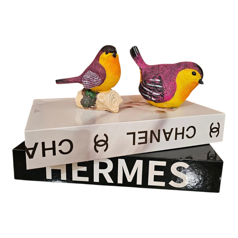 Home Sajawat decorative resin bird figurines with vibrant purple and yellow hand-painted details on a book stack.
