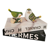 Home Sajawat decorative resin bird figurines with green and yellow hand-painted details perched on stacked books.