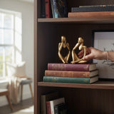 Home Sajawat gold abstract thinker statues displayed on a bookshelf with books, held by a hand.