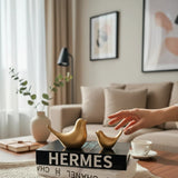 Home Sajawat set of two matte gold bird figurines displayed on designer coffee table books in a modern living room