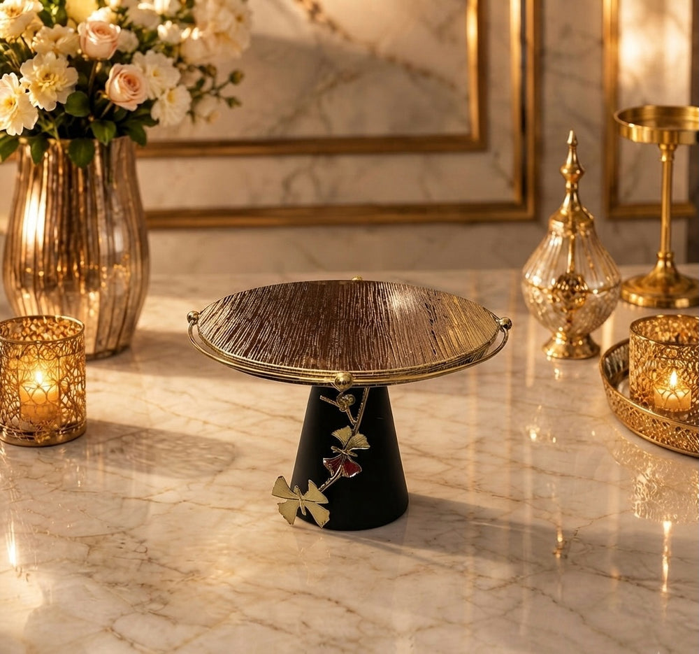 Home Sajawat decorative cake stand with a textured gold plate, matte black base, and elegant ginkgo leaf detailing.