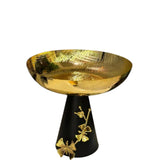 Home Sajawat decorative gold fruit bowl with hammered texture on a black pedestal base with gold floral and butterfly motifs.