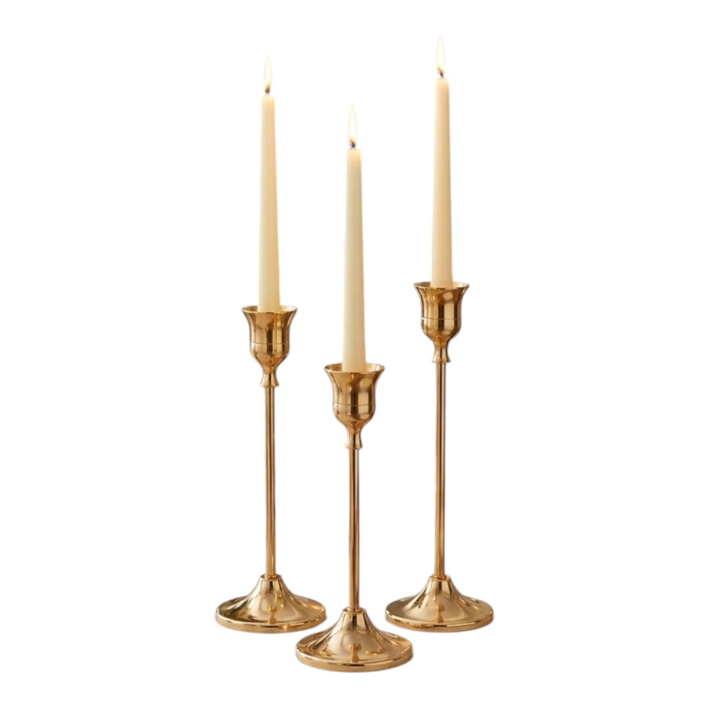 Home Sajawat set of three gold metal candlesticks with cream taper candles on a dining table.