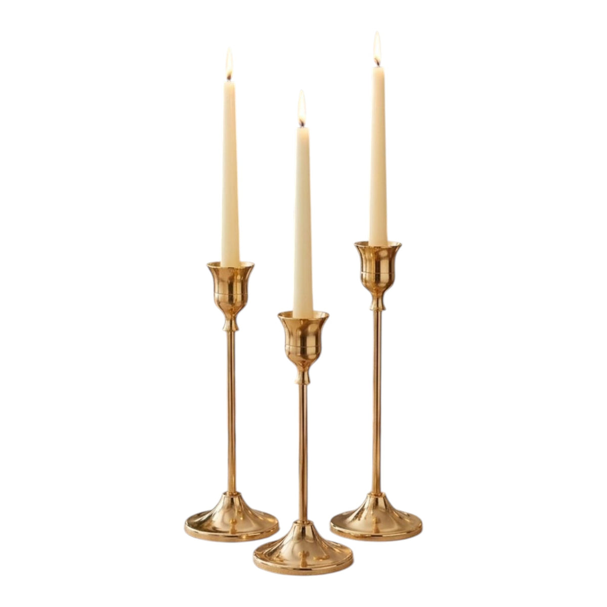 Home Sajawat set of three gold metal candlesticks with cream taper candles on a dining table.