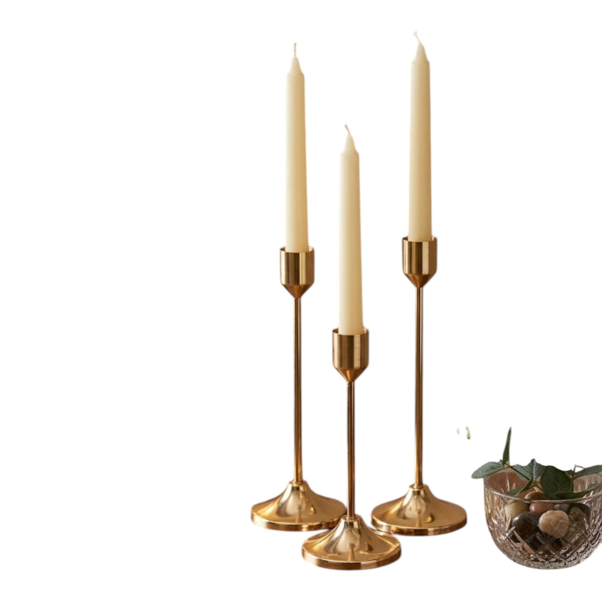 Home Sajawat set of three gold metal candlesticks with cream taper candles on a wooden table.