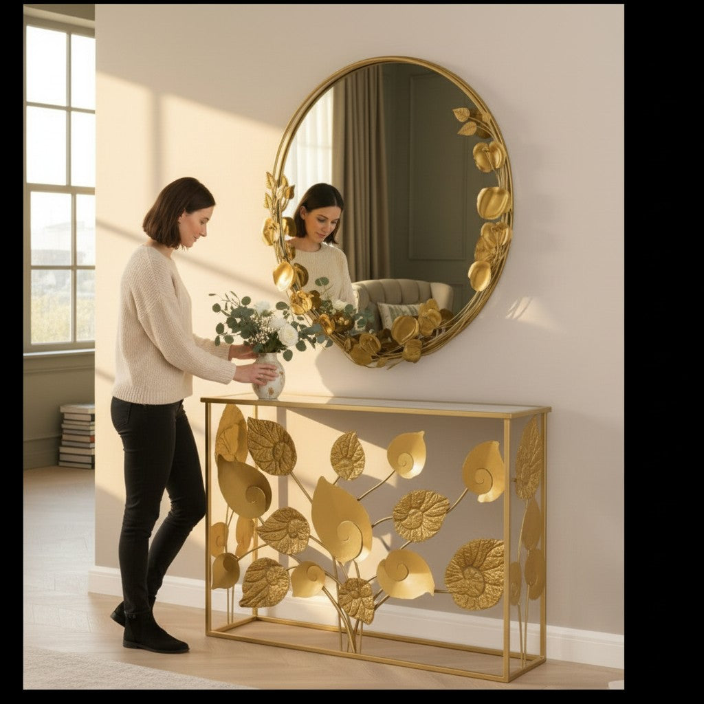 Woman styling a Home Sajawat gold metal floral console table and matching round leaf-adorned wall mirror in a hallway.