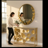 Woman styling a Home Sajawat gold metal floral console table and matching round leaf-adorned wall mirror in a hallway.