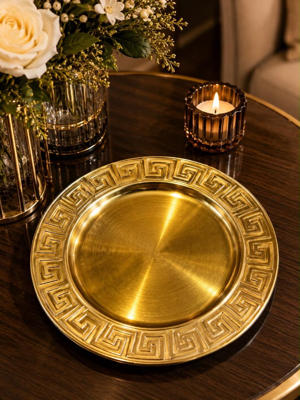 Home Sajawat gold charger plate with a classic Greek key border design on a dark wooden dining table.