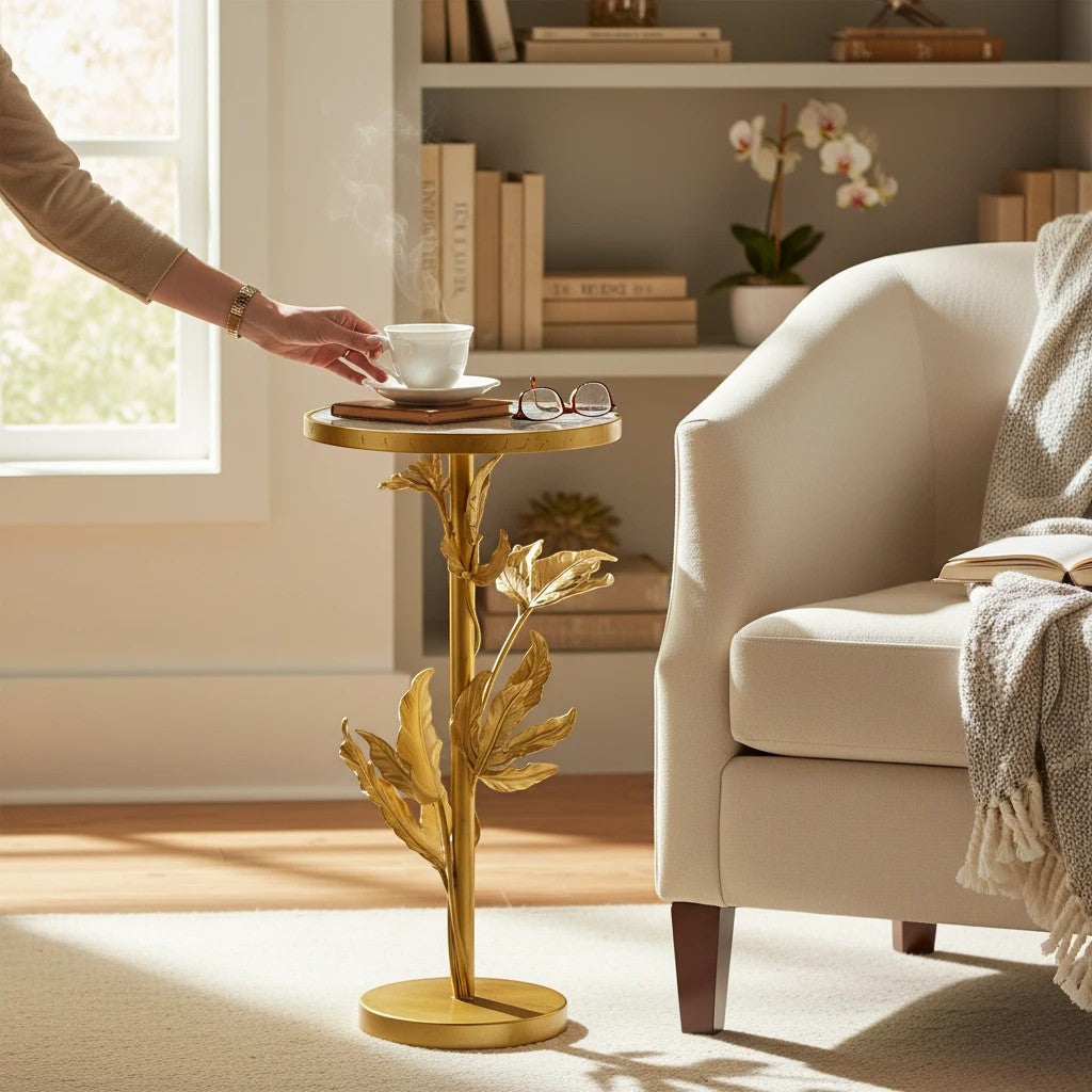 Home Sajawat gold leaf accent table with round white crackled top and ornate stem, next to a cream armchair.
