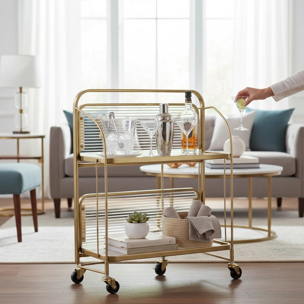 Home Sajawat gold metal two-tier bar cart with clear acrylic shelves and ribbed panels, on wheels.