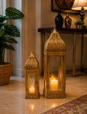 Home Sajawat set of two ornate gold metal Moroccan-style lanterns with intricate filigree and glowing pillar candles.