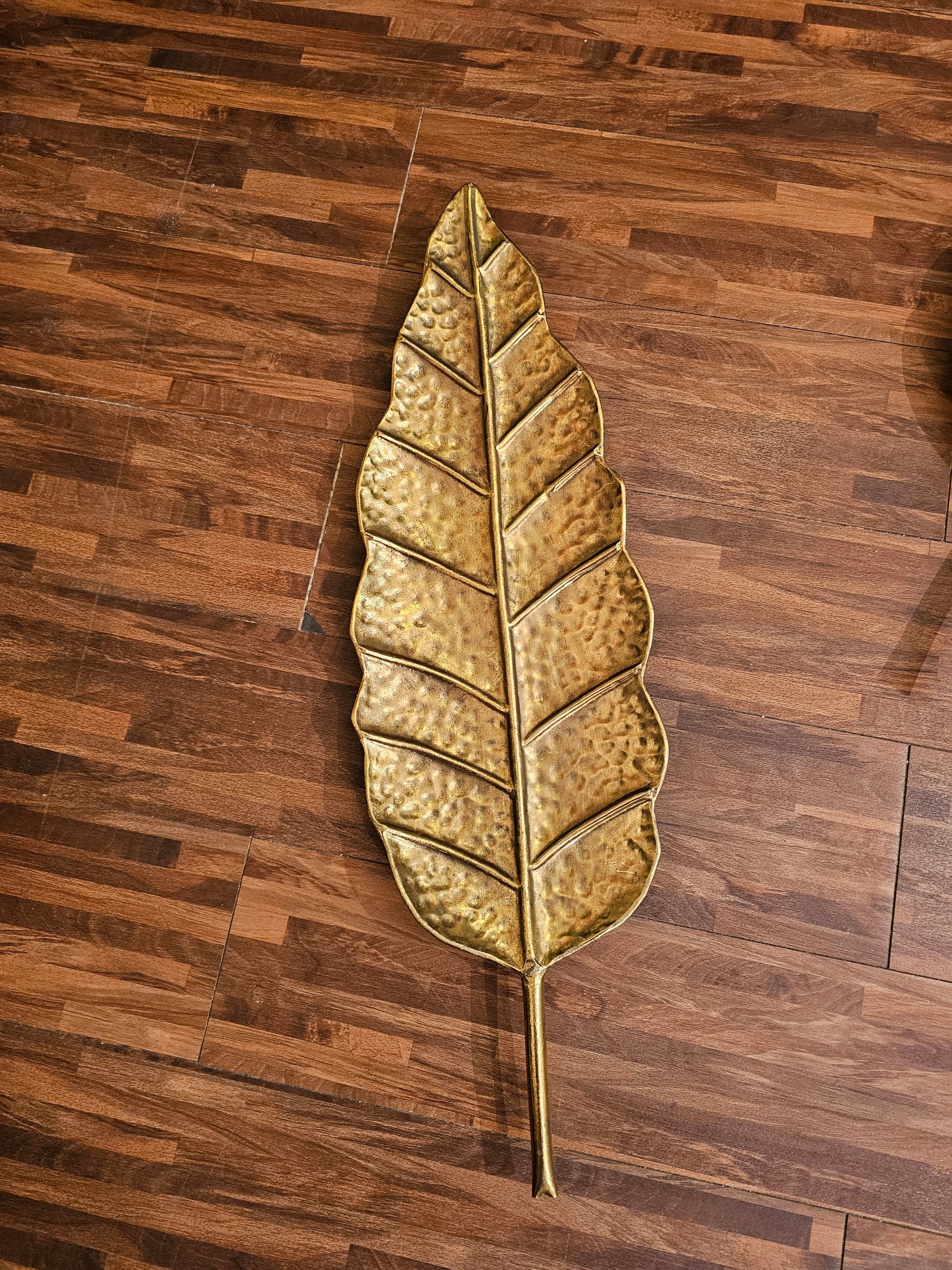 Home Sajawat gold metal leaf tray with hammered texture and intricate vein detailing on a wooden floor background.