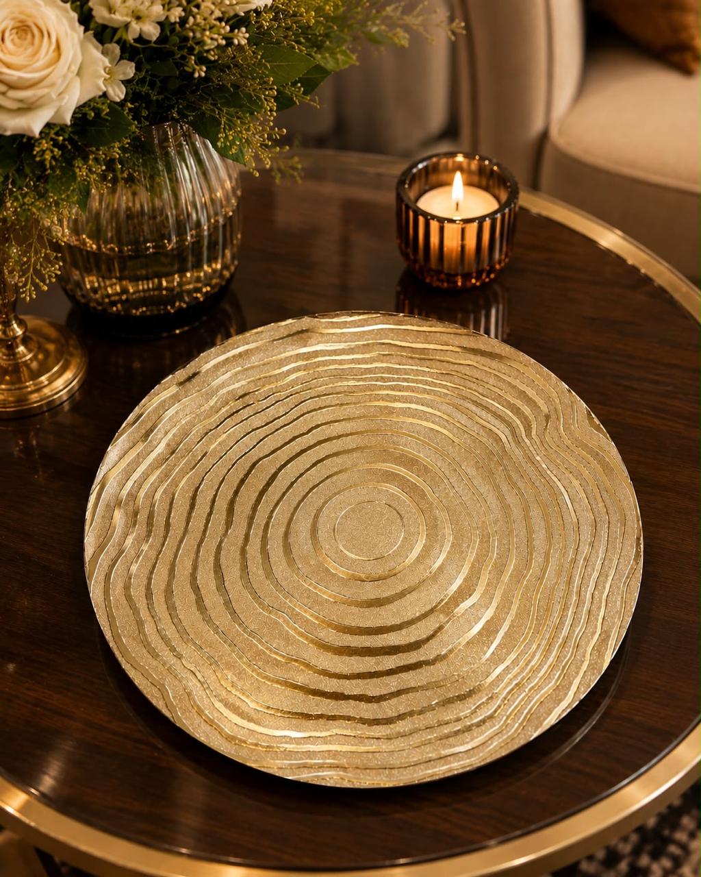 Home Sajawat gold charger plate with a textured concentric circle design on a dark wood table with a candle and flowers