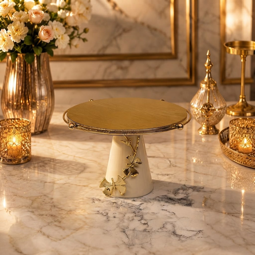 Home Sajawat decorative cake stand with a brushed gold plate, white ceramic base, and gold butterfly embellishment.