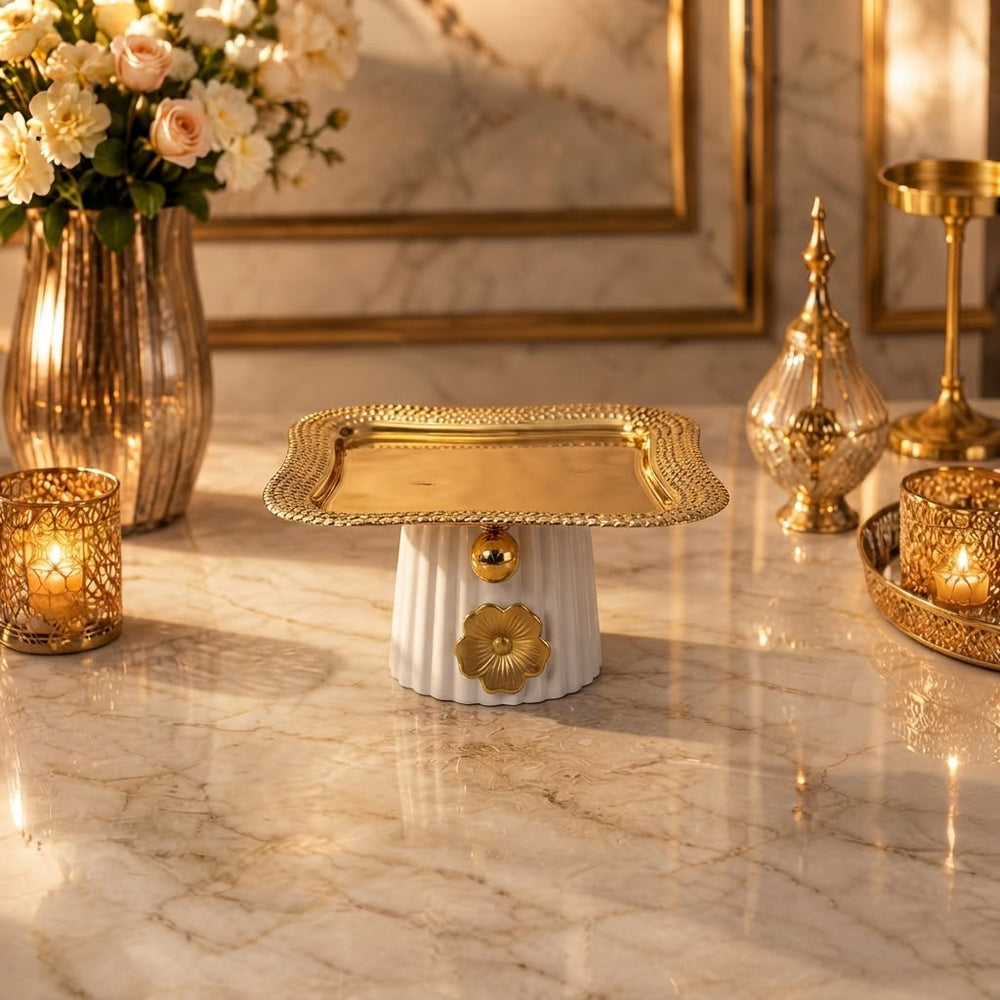 Home Sajawat decorative pedestal serving tray with a polished gold-tone metal top and a white fluted ceramic base.