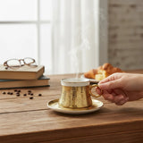 Home Sajawat hammered gold ceramic coffee cup and saucer set with white interior and gold handle.