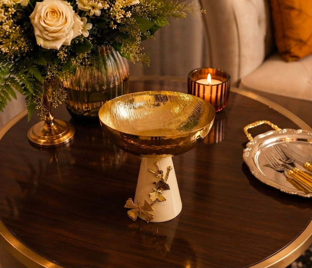 Home Sajawat decorative pedestal bowl with a hammered gold-tone finish and a cream ceramic base with ginkgo accents.